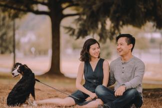 Two people sitting on the ground with a white and black dog on a leash
